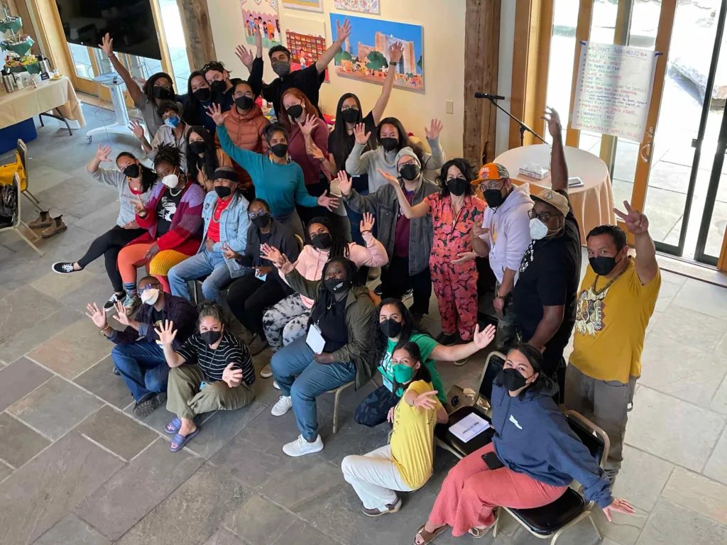 Group of people sitting and standing indoors. They're masked and raising their hands in celebration.